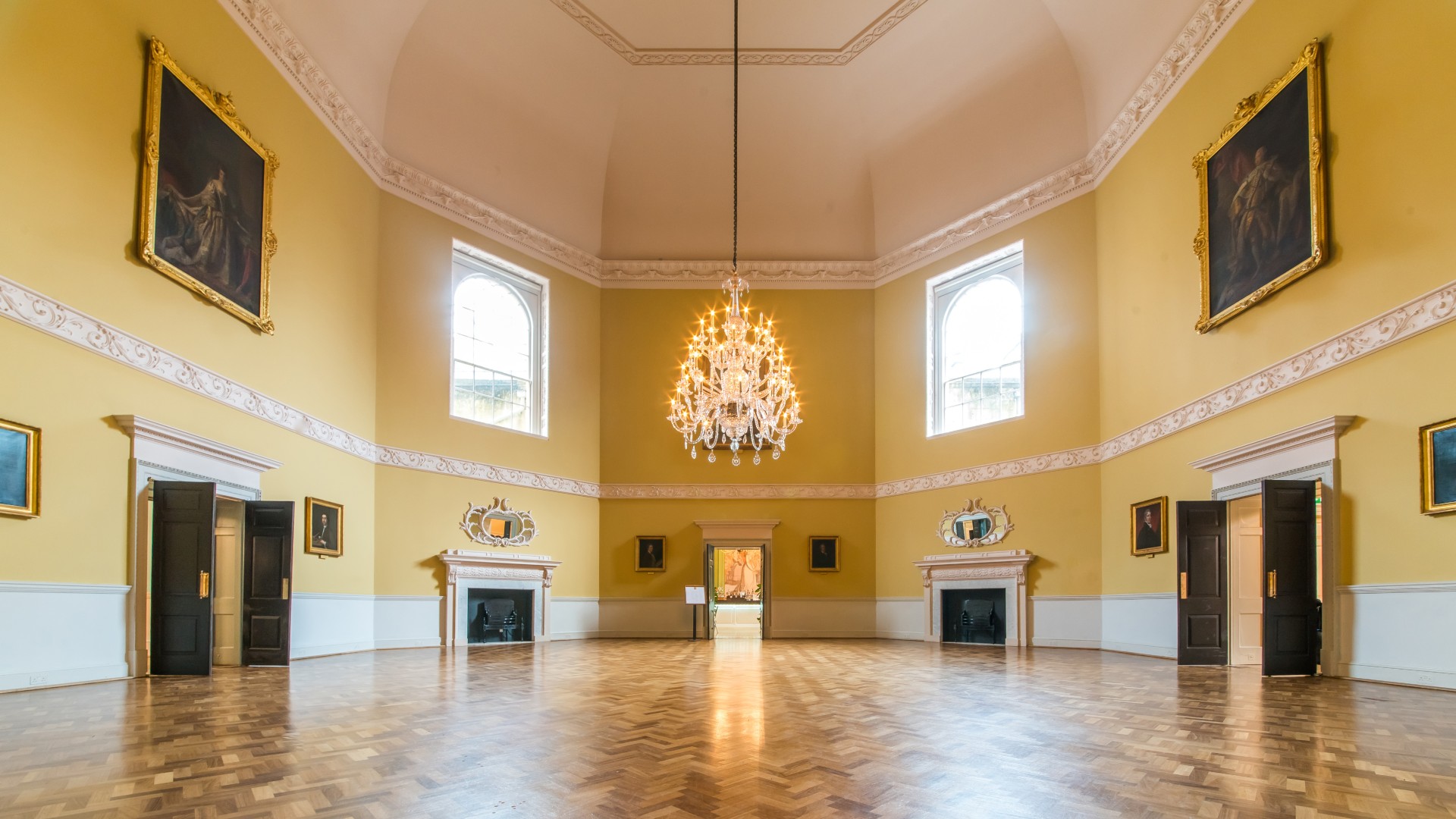 An empty room, painted yellow, decorated with a chandelier and paintings